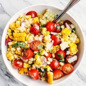 Fresh summer corn and tomato salad with cherry tomatoes, red onion and basil in a white bowl