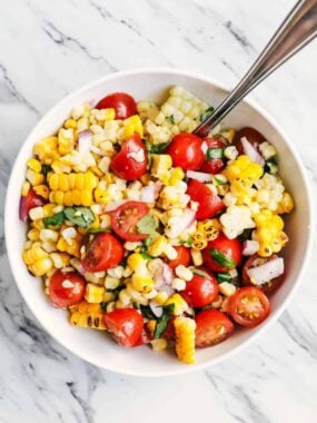 Fresh summer corn and tomato salad with cherry tomatoes, red onion and basil in a white bowl