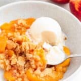 Peach cobbler and ice cream in a bowl with spoon.