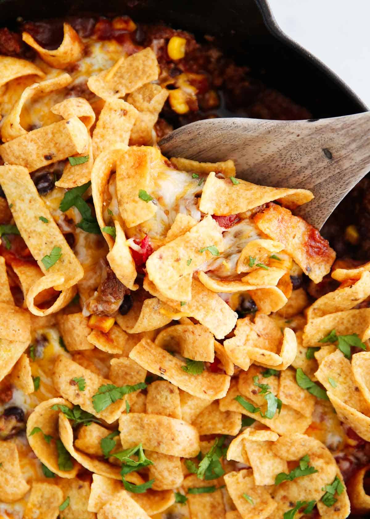 Close up of frito pie in skillet with a serving spoon.