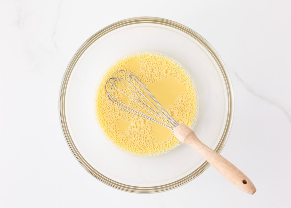 Whisked milk, eggs, water, and vanilla in a glass bowl, the wet base for funnel cake batter.