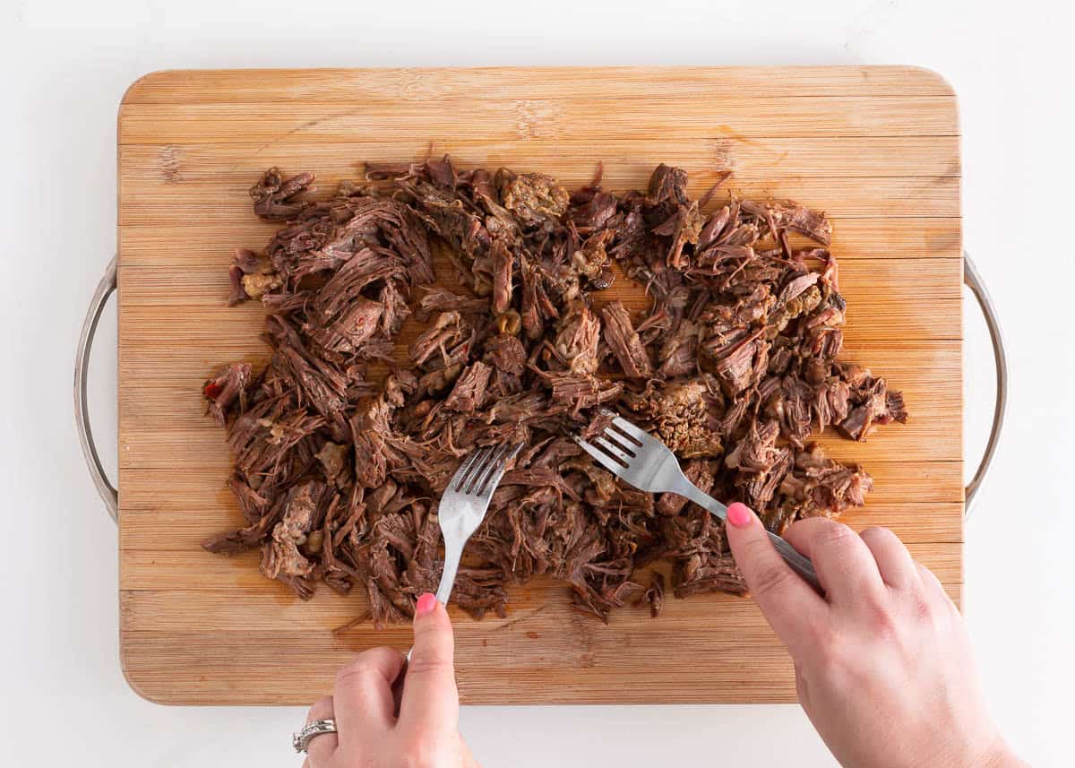 Shredding birria beef on a cutting board.