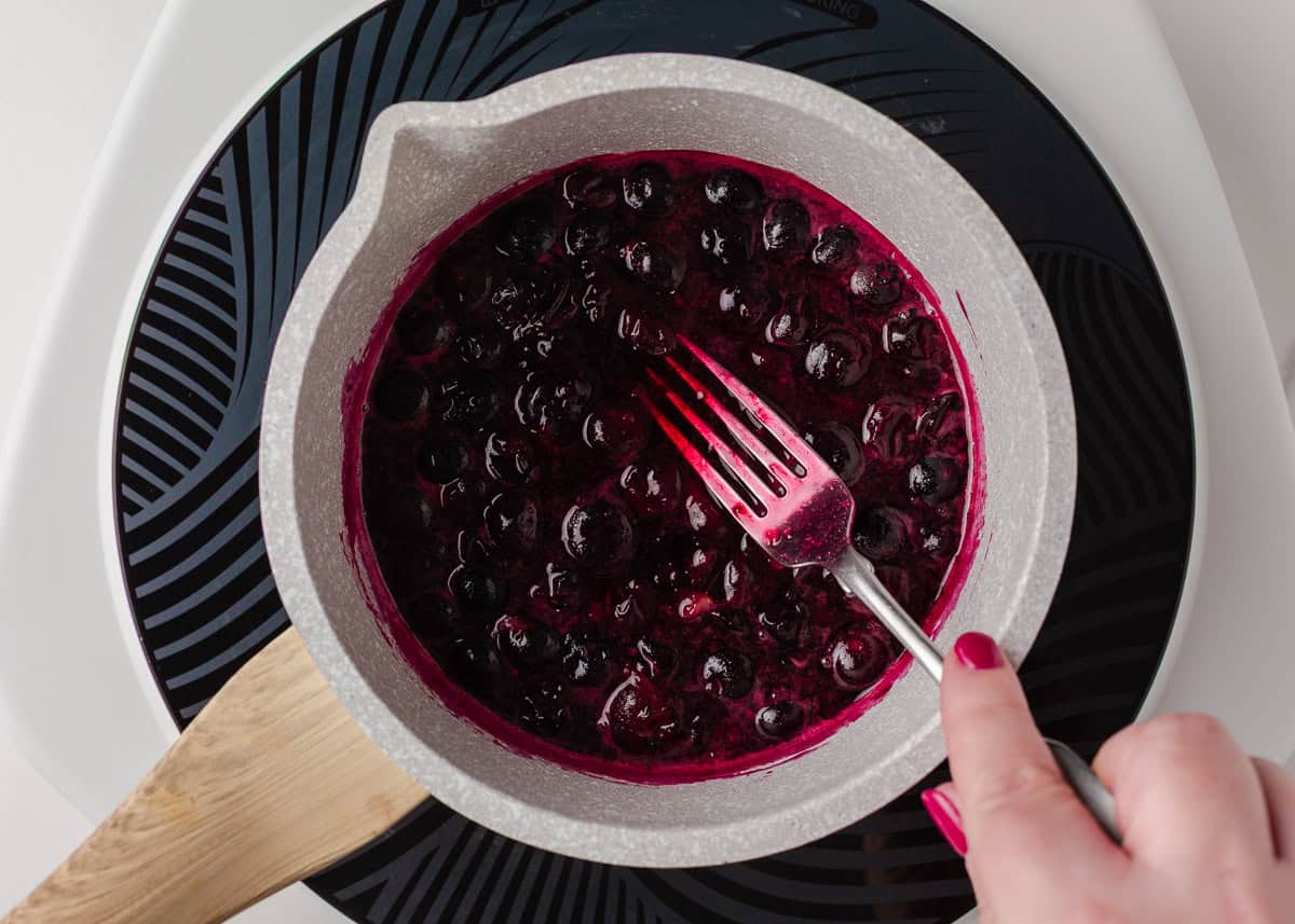 Blueberry sauce for crepes simmering in a saucepan as the berries burst and thicken.