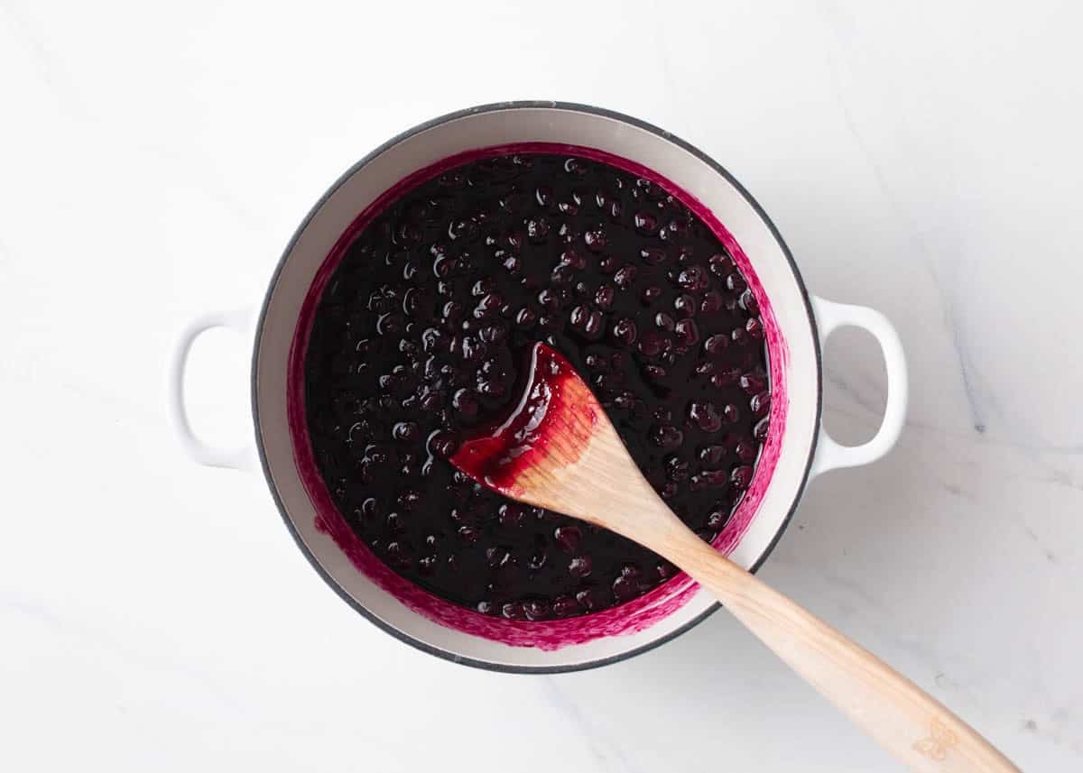 Thickened blueberry jam in a saucepan with a wooden spoon.