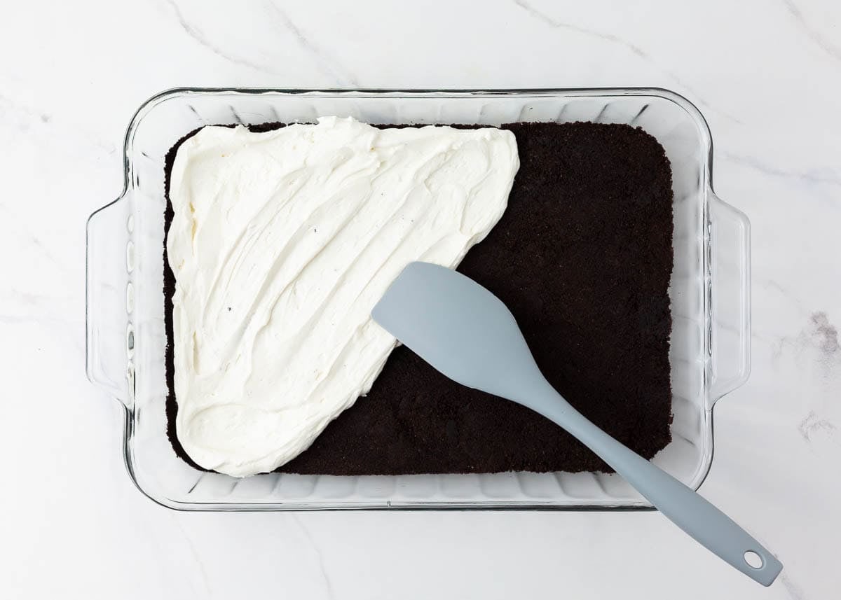 Spreading creamy cheesecake layer over Oreo crust.