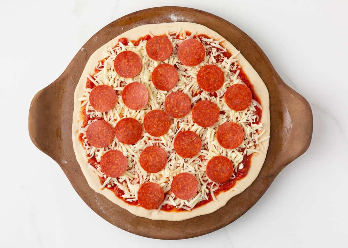 Unbaked homemade pepperoni pizza topped with pizza sauce, shredded mozzarella cheese, and sliced pepperoni on a pizza pan.