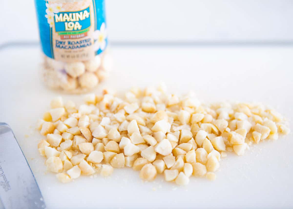 Macadamia nuts scattered on a chopping block cut into wedges with a knife on the side.