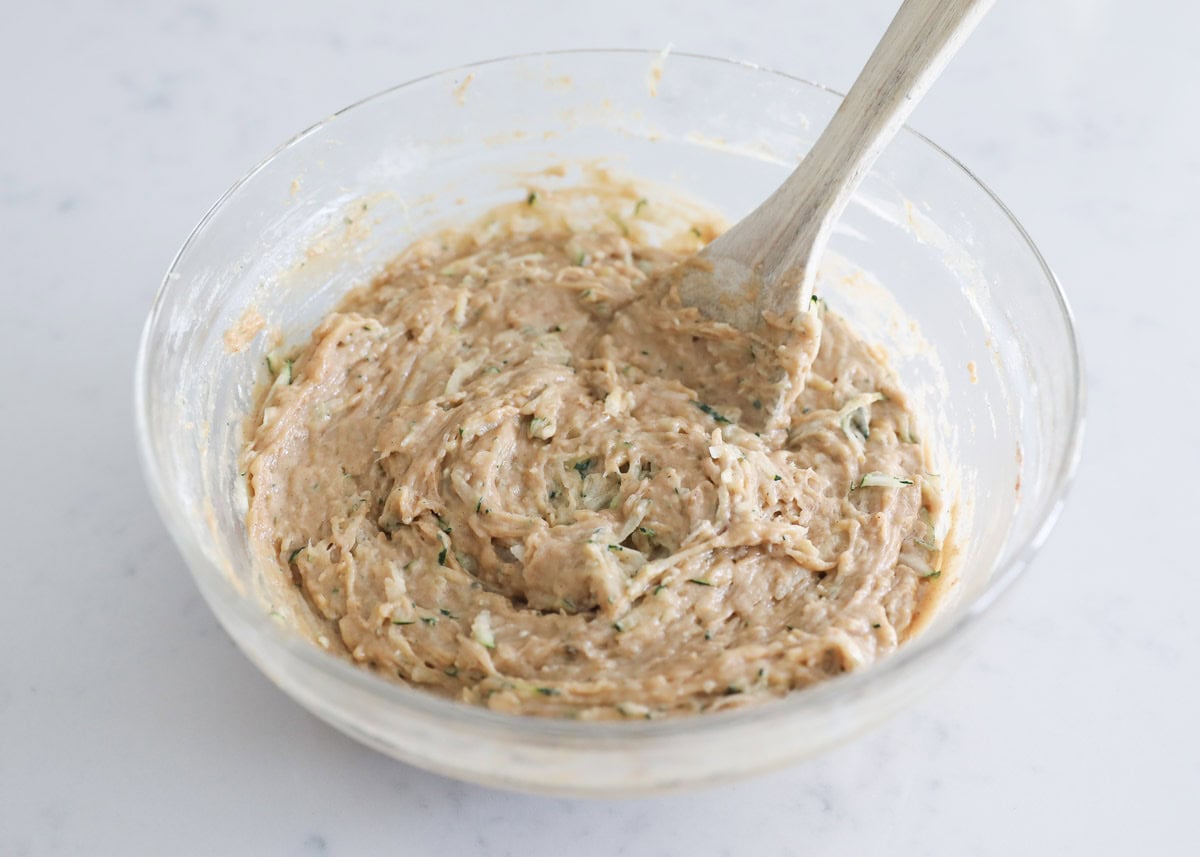 Banana zucchini muffin batter being stirred in a large bowl with grated zucchini just folded in.