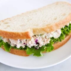 Tuna salad made into a sandwich on white bread served on a white plate.