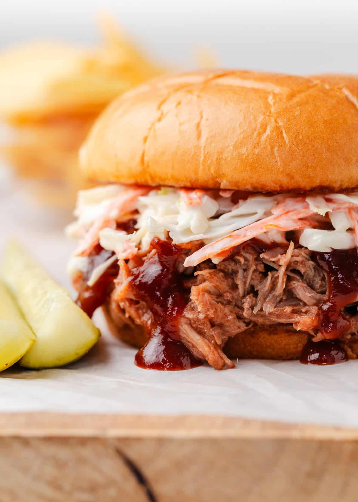 Tender shredded pulled pork smothered in tangy BBQ sauce and served on a toasted hamburger bun. This BBQ pork sandwich recipe is an easy, no-fail dinner idea that takes just 5 minutes to prep! BBQ pulled pork sandwich topped with coleslaw and barbecue sauce on a soft bun, served with pickle slices.