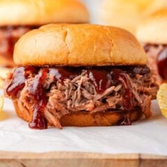 Close-up of BBQ pulled pork sandwiches on soft buns with juicy shredded pork and barbecue sauce, served with potato chips.