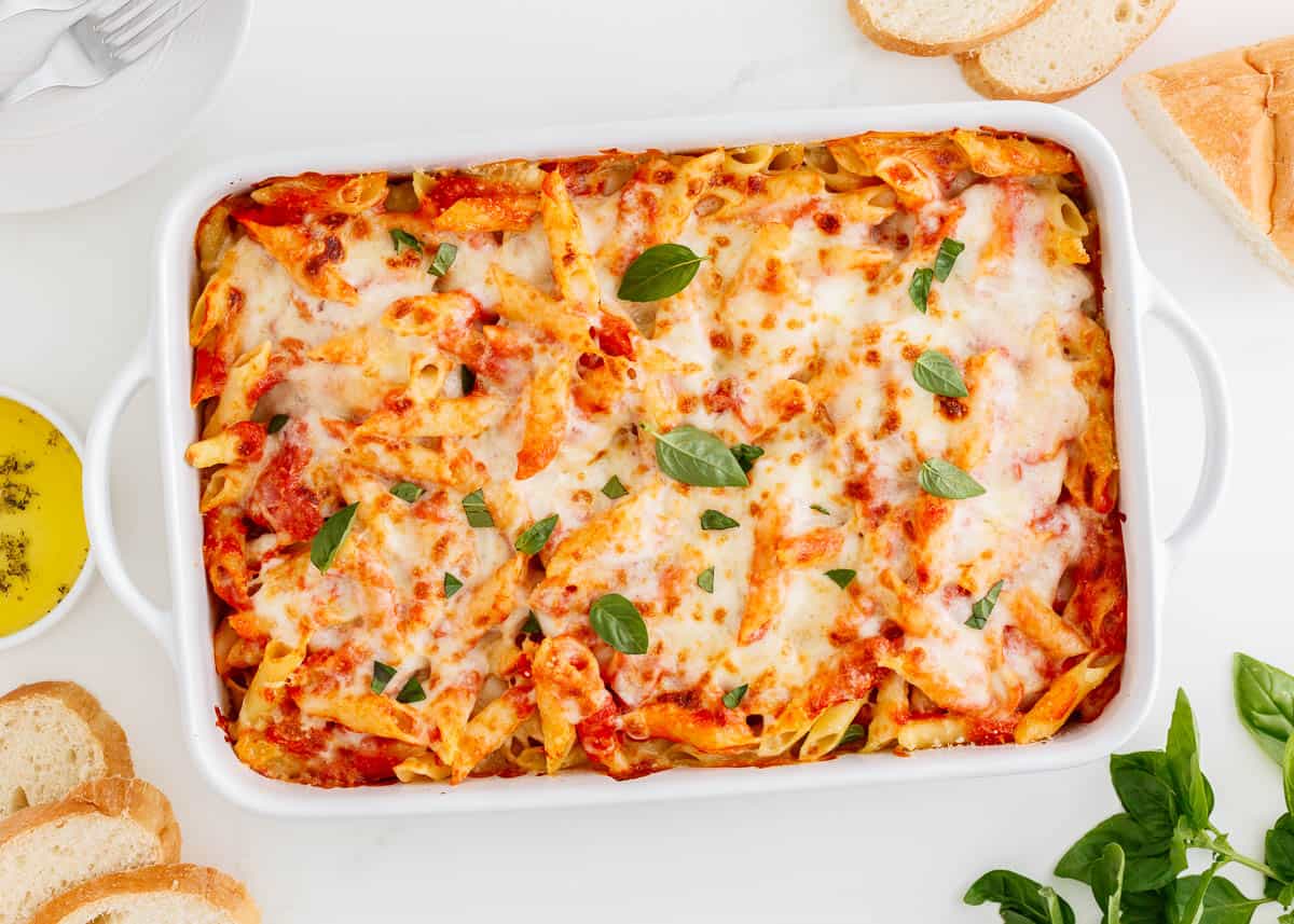 Layers of Mostaccioli pasta, San Marzano tomatoes, melted mozzarella, and Parmesan cheese come together in this Italian-inspired baked mostaccioli ready for serving your family and guests a wholesome flavorful meal! Baked mostaccioli in a white dish.