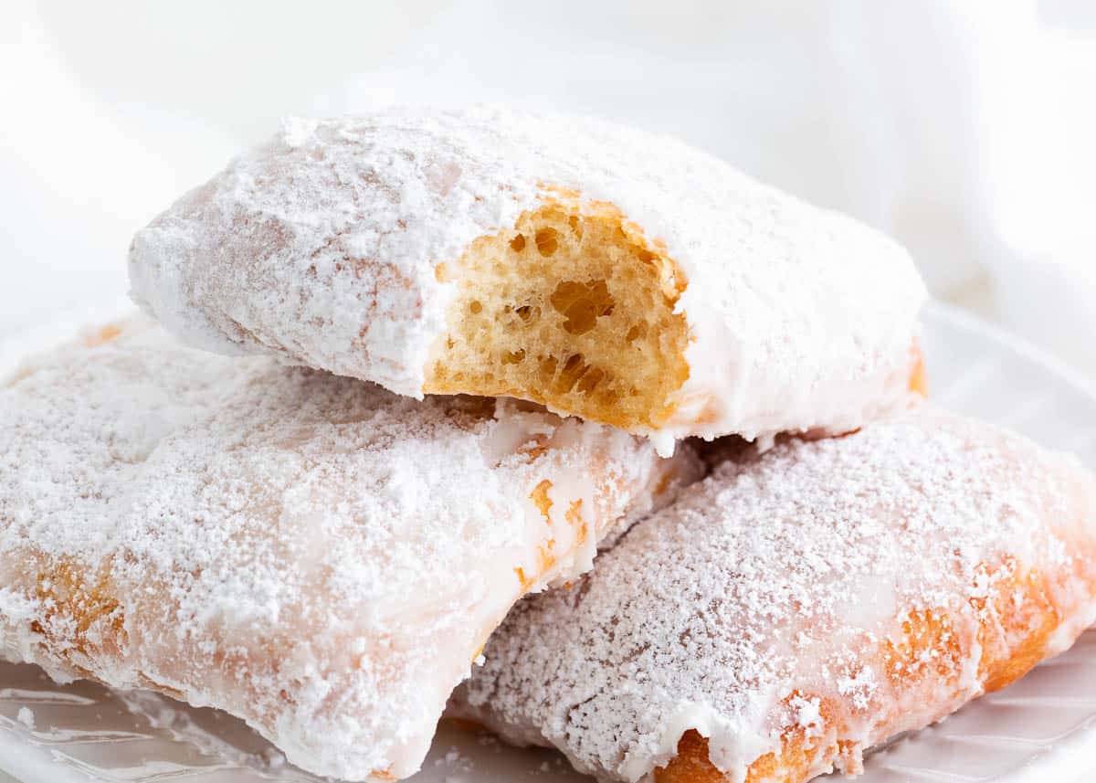 Beignets stacked on a white plate with a bite taken.