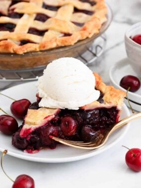 A slice of cherry pie on a plate with ice cream and a fork.