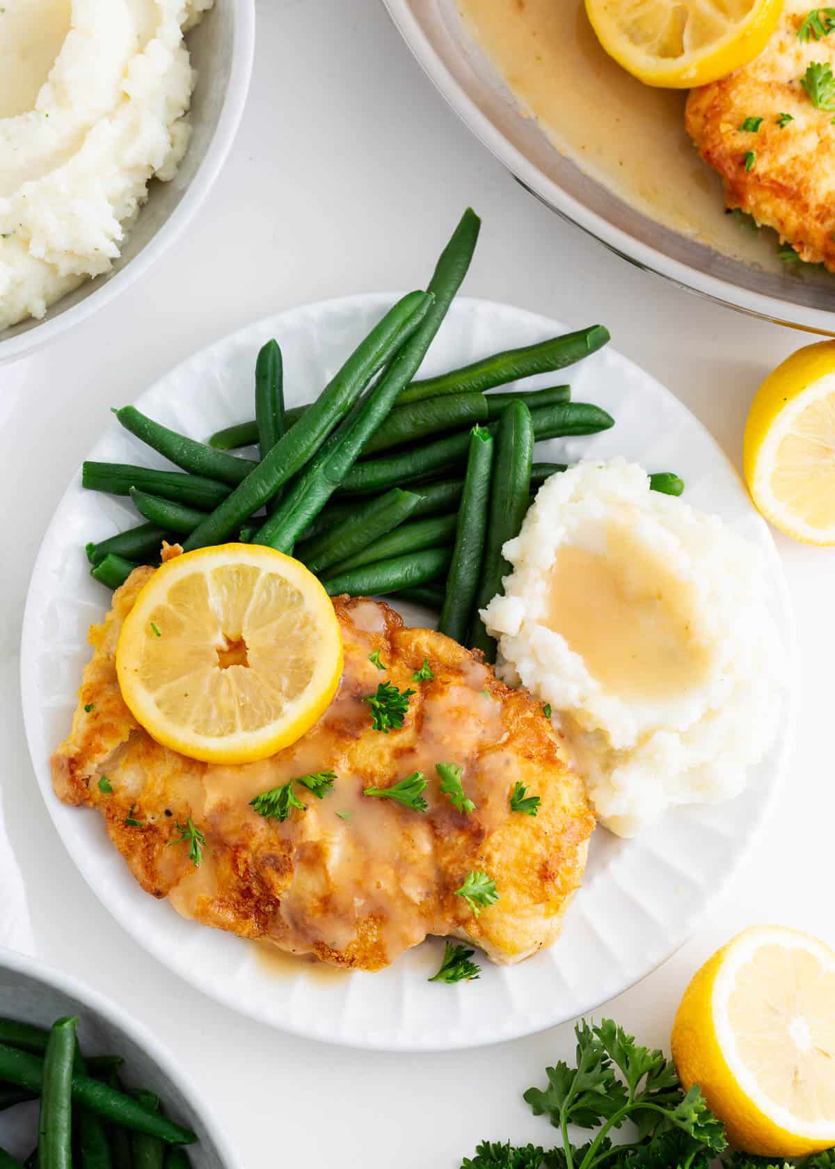 Chicken francese on a plate with mashed potatoes and green beans. 