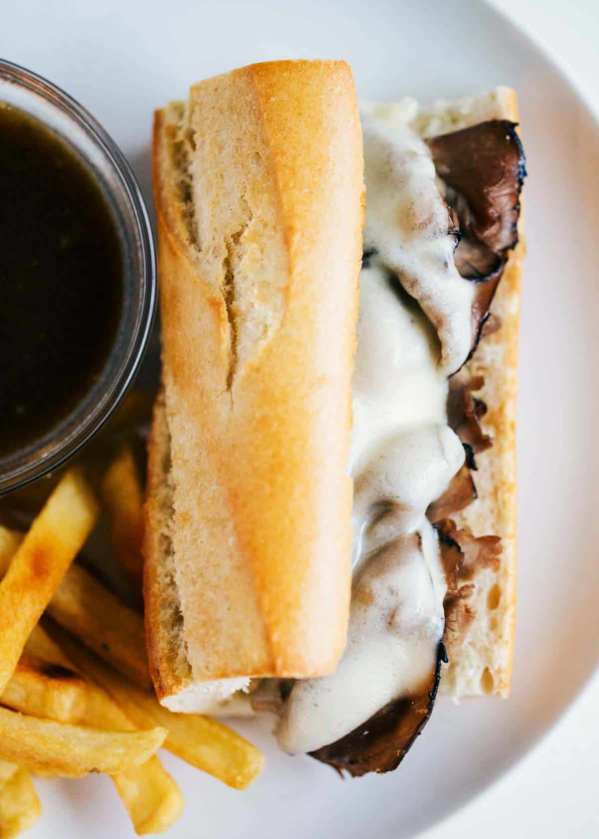 French dip sandwiches on a white plate next to au jus. 