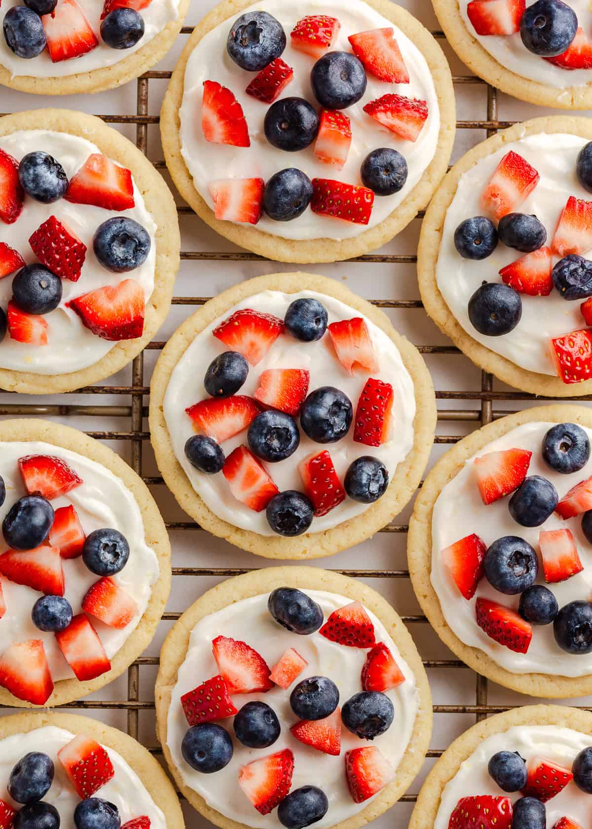 Looking for easy 4th of July desserts options to take along to your family BBQ or Independence Day celebration? These all-American summertime treats are made with patriotic red, white and blue colors, are quick to make and most importantly, delicious! Fruit pizza cookies on a wire rack.