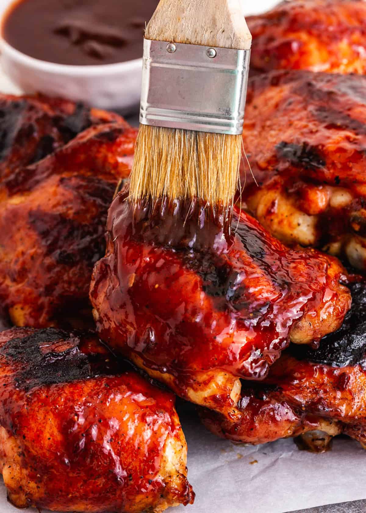 Grilled BBQ chicken pieces being basted with sauce.