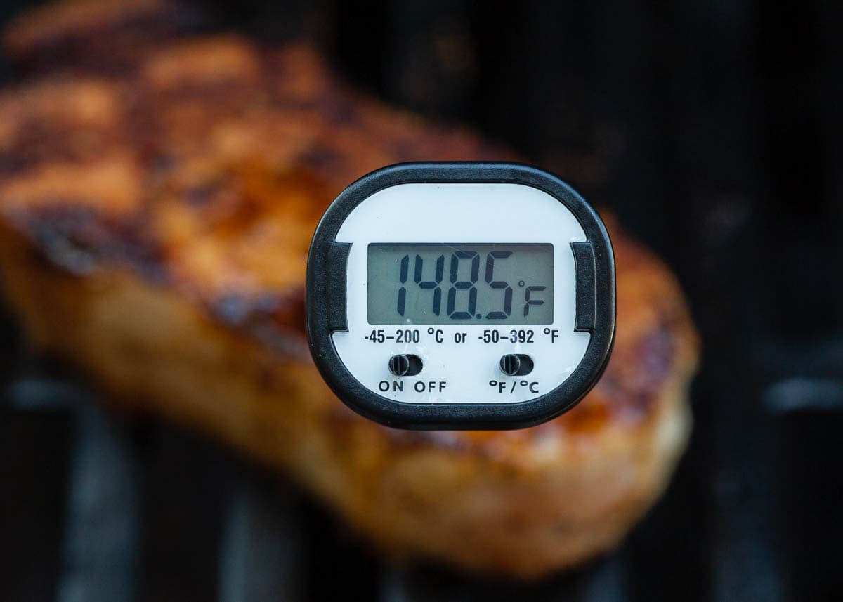 A pork on the grill with a digital thermometer showing optimal doneness.