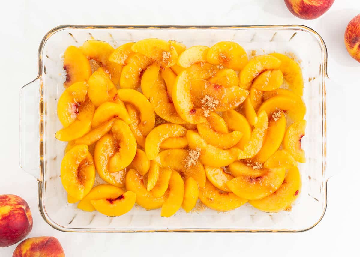 Sliced peaches in baking dish sprinkled with brown sugar.