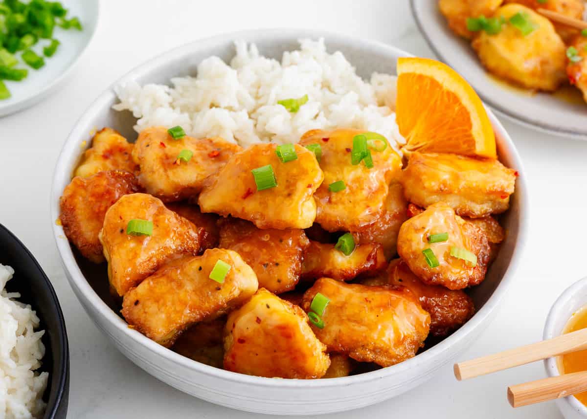 Orange chicken and rice in a white bowl.