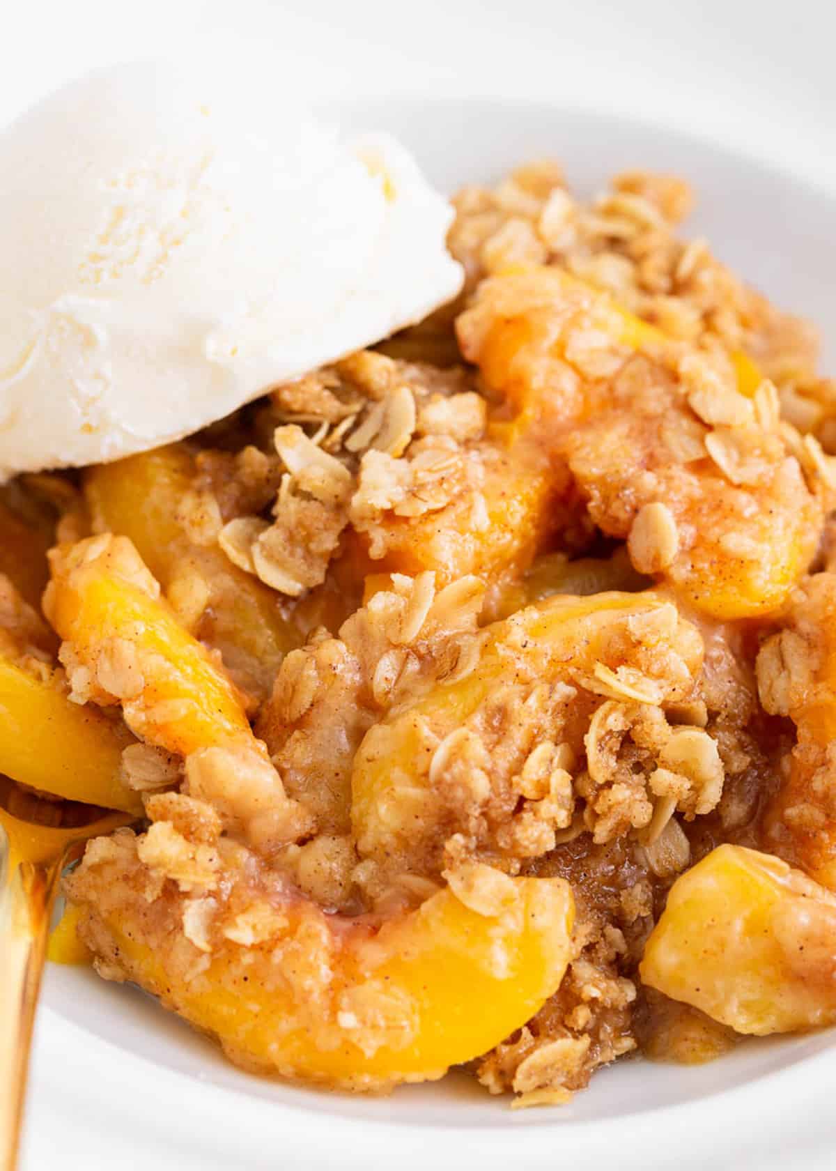 Peach crisp in a white bowl with ice cream.