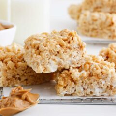 Stack of peanut butter rice krispie treats on metal rack with extra peanut butter on a spoon.