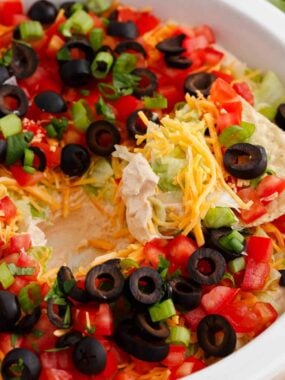 Dipping a tortilla chip into taco dip with cream cheese.