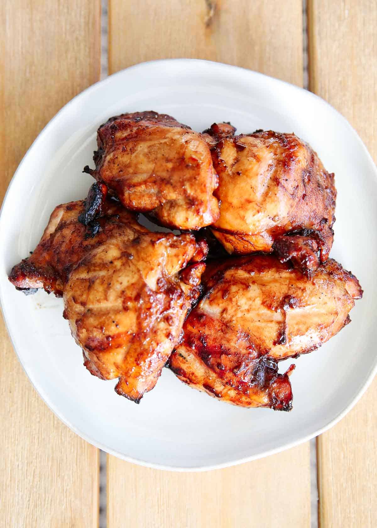 A pile of grilled chicken thighs on a white plate. 