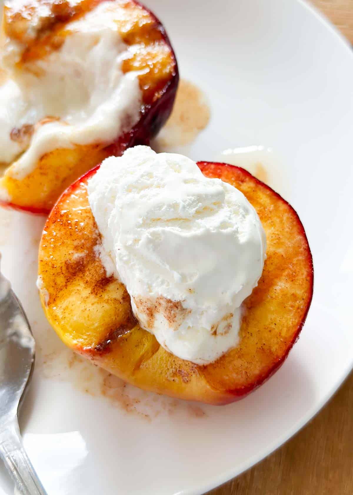 Grilled peaches on a plate with whipped cream.