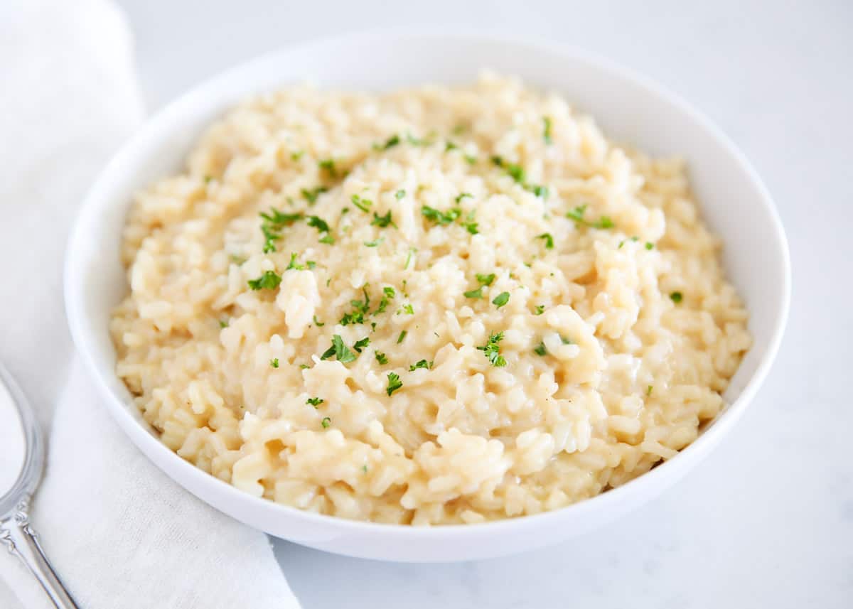 Learn to make rich and creamy restaurant-style risotto with easy steps and simple ingredients. Cooked low and slow in chicken broth, white wine if desired, with tons of Parmesan cheese and butter added for flavor and texture, then topped with fresh herbs. This is the BEST risotto recipe you'll ever need! Risotto in a white bowl.