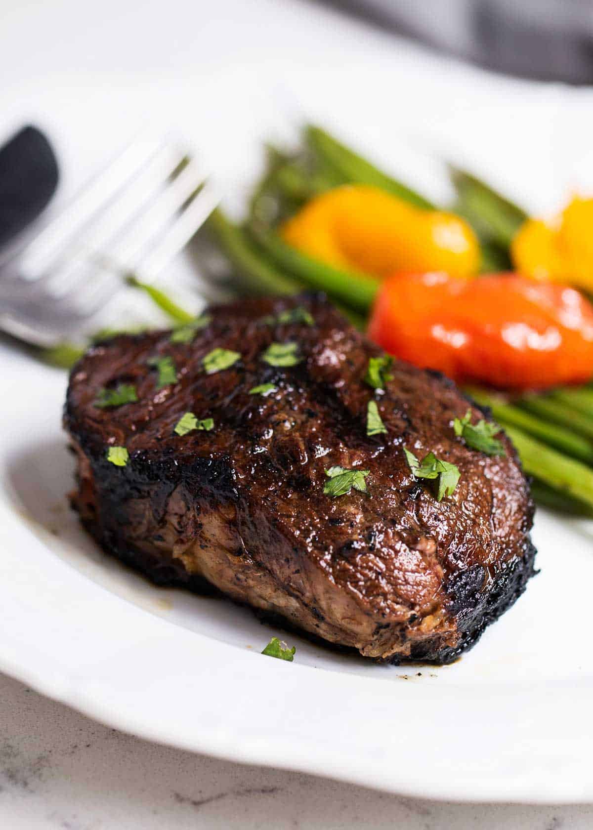 Steak on a white plate with vegetables on the side. 