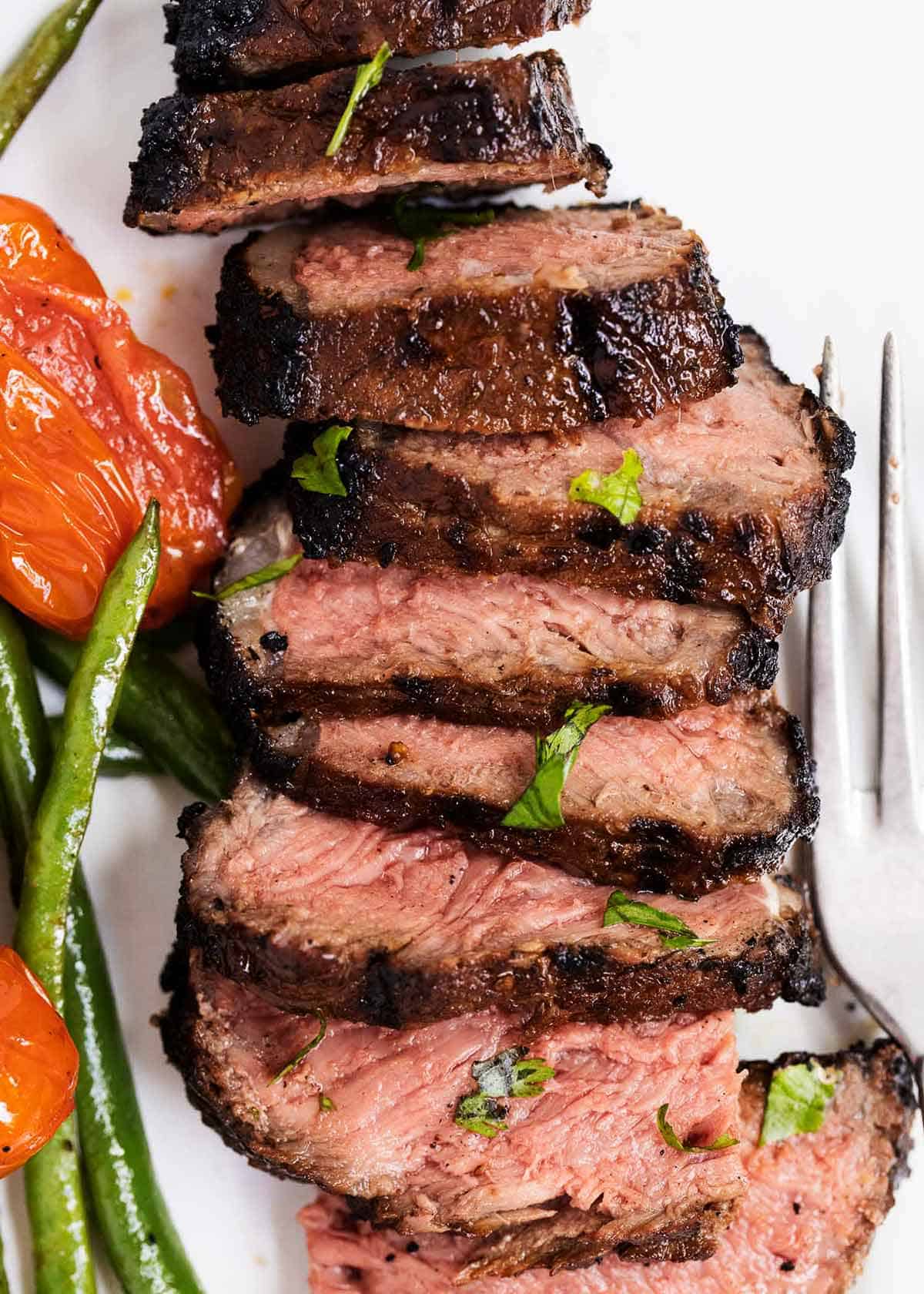 Sliced steak on a cutting board with grilled vegetables on the side. 