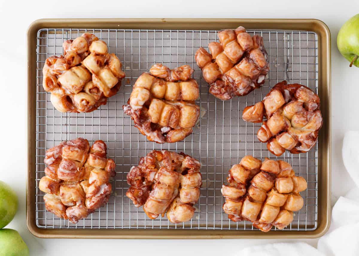 Apple fritters with glaze on a cooling rack.