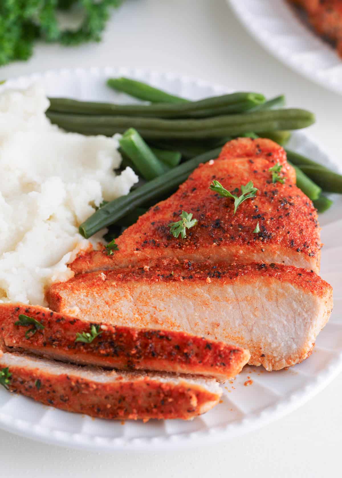 Sliced baked pork chops on a plate with mashed potatoes and green beans.