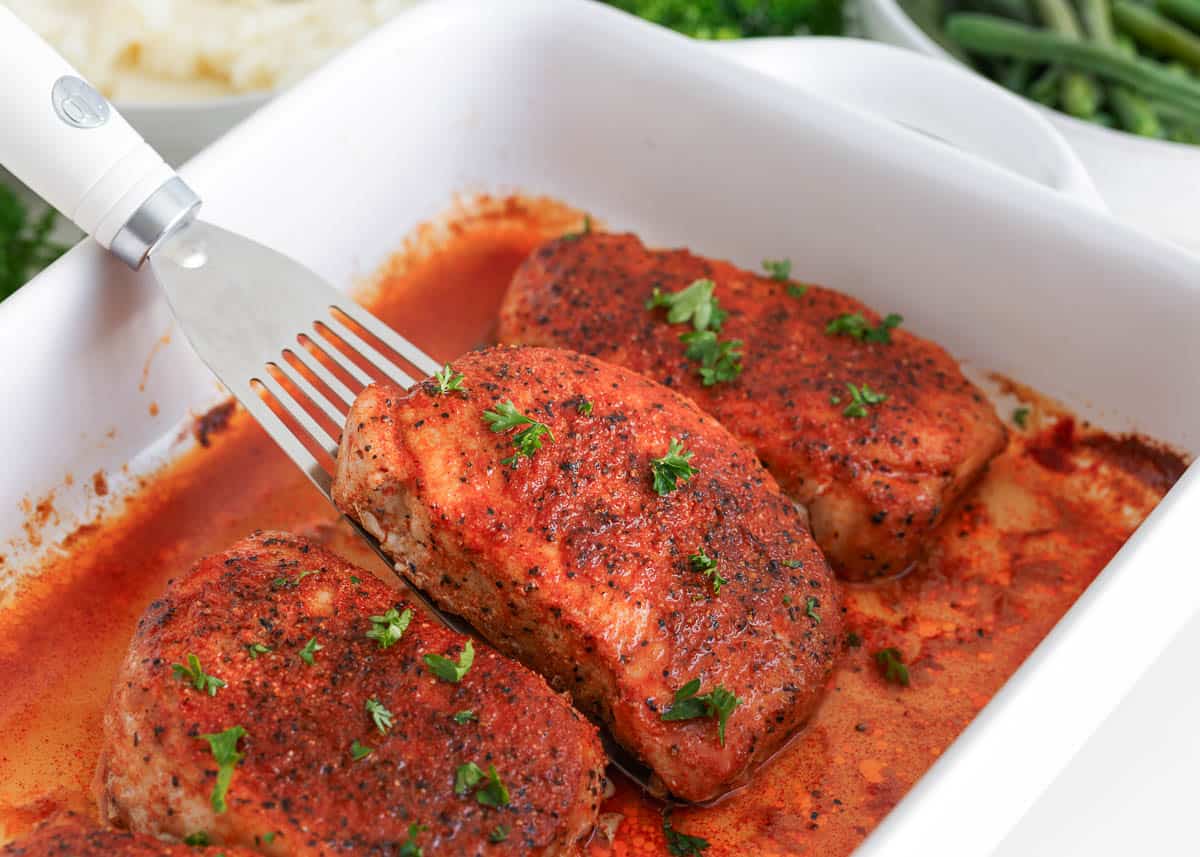 Baked pork chops in a white baking dish.
