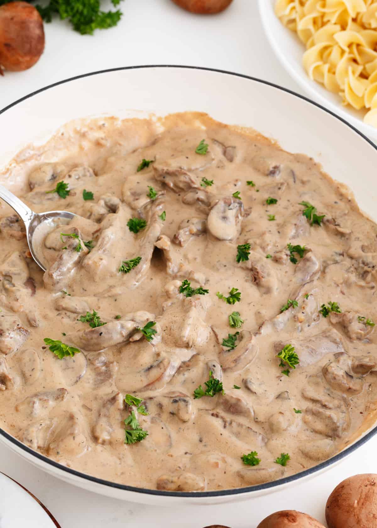 Beef stroganoff cooking in a white pot.