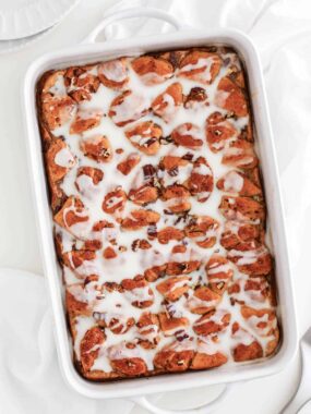 Cinnamon roll casserole drizzled with icing and resting on counter.