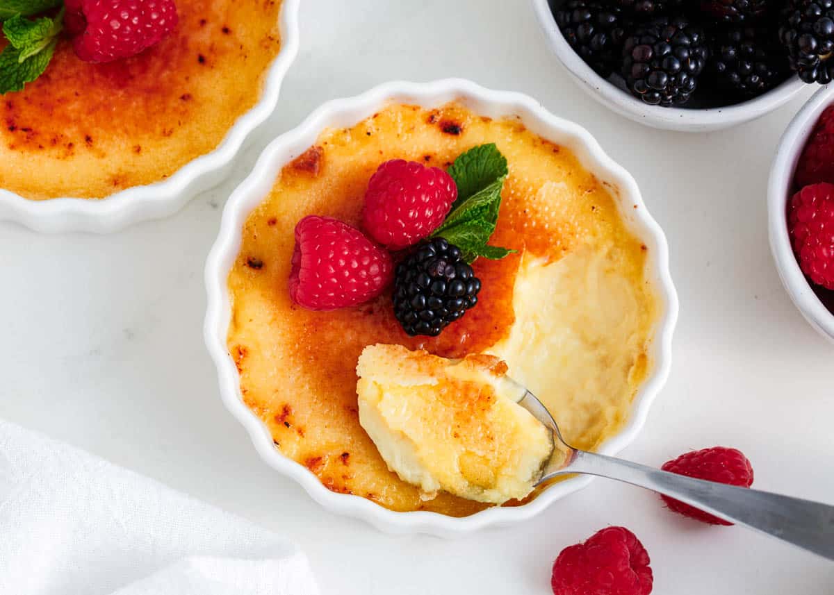 Creme brulee baked in a white dish with berries on top.