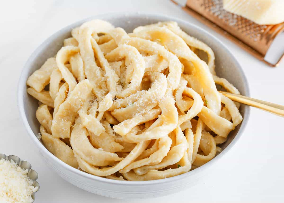 Fresh, soft, and tender homemade egg noodles are easy to make with just 3 ingredients and ready to serve in 30 minutes! Flour, eggs, and water make this simple dough without the need for a pasta maker, so it can all be done by hand! Homemade egg noodles in a bowl with parmesan.