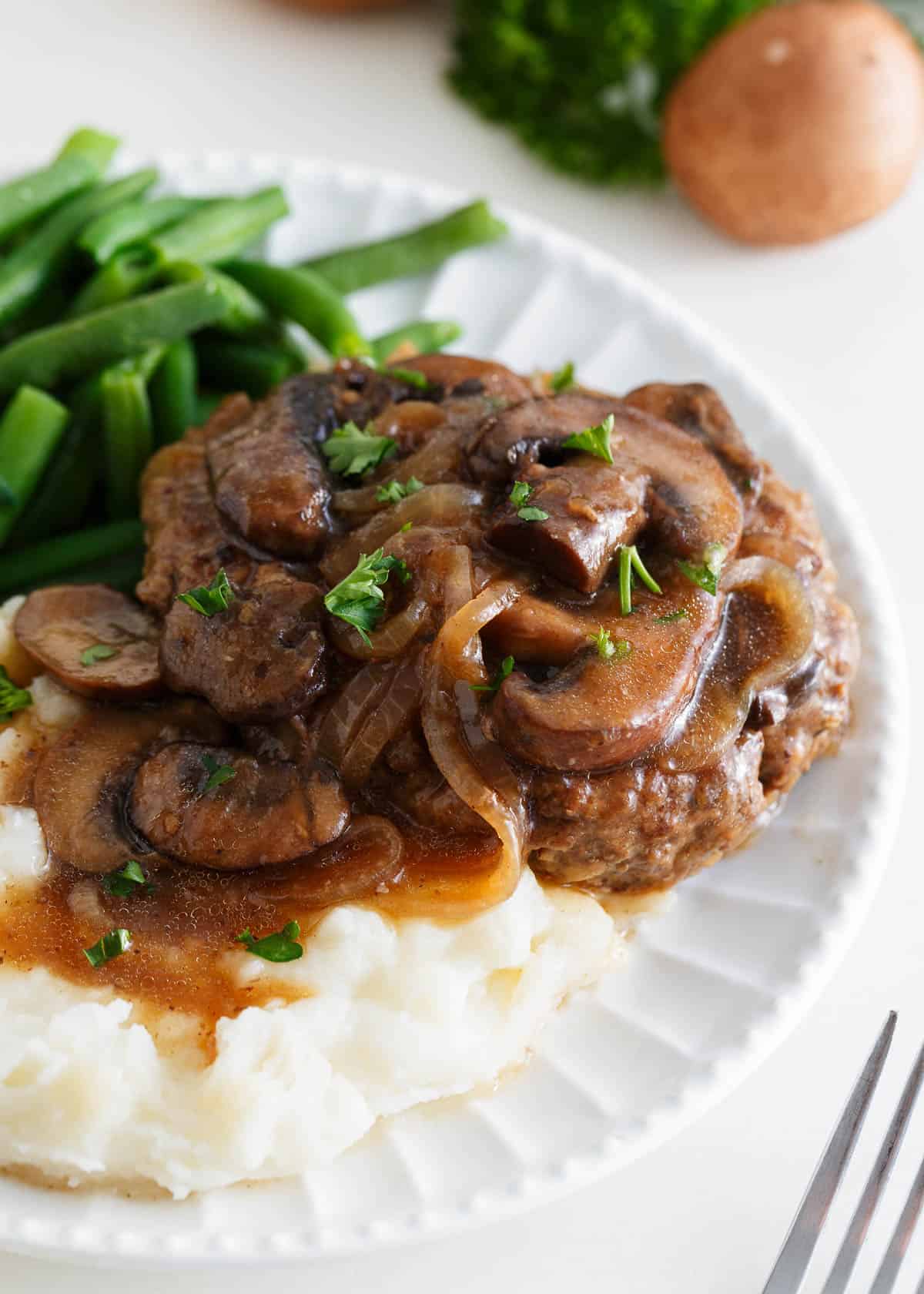 Salisbury steak on a white plate with mashed potatoes.