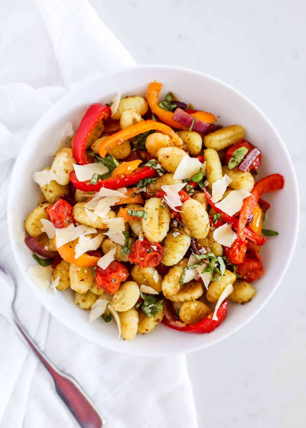 A white bowl with gnocchi and vegetables. 