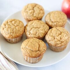 Applesauce muffins on a white plate with an apple and slices in the background.