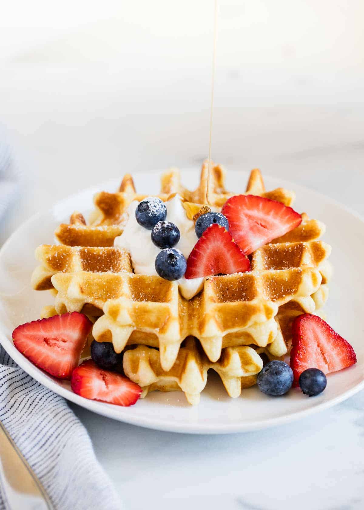 Belgian waffles stacked on top of each other on a white plate topped with berries. 