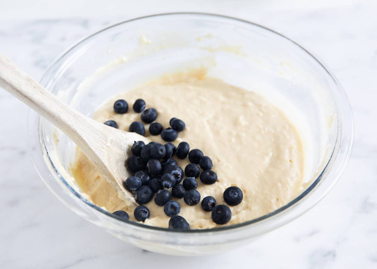 Blueberry batter in a glass bowl with a wooden spoon. 