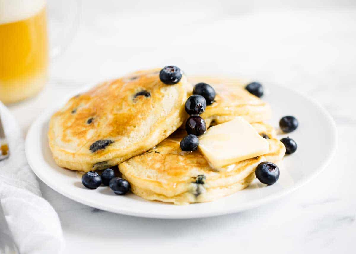 Blueberry pancakes stacked on top of each other on a white plate. 