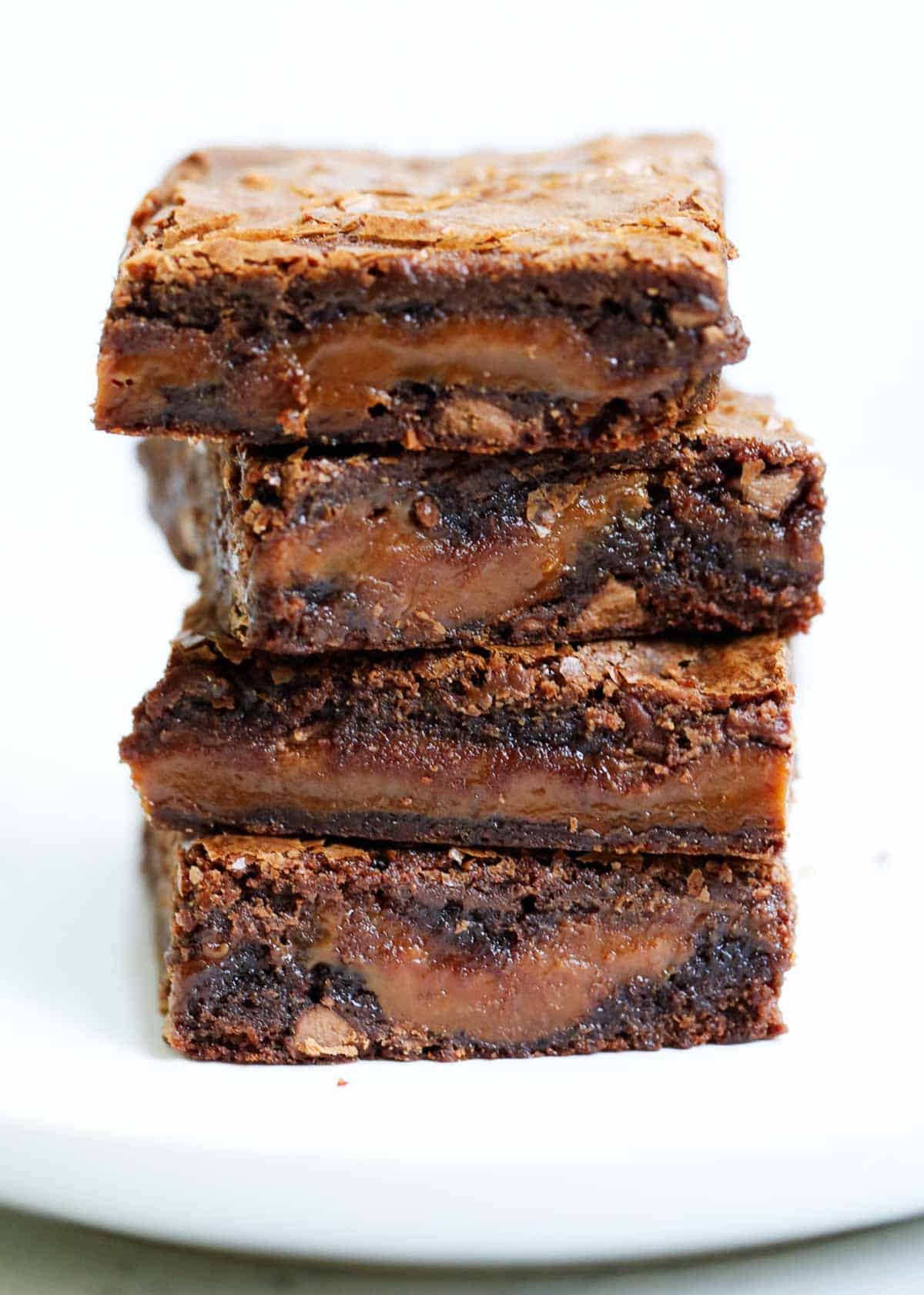 Four caramel brownies stacked on top of each other with a white background. 
