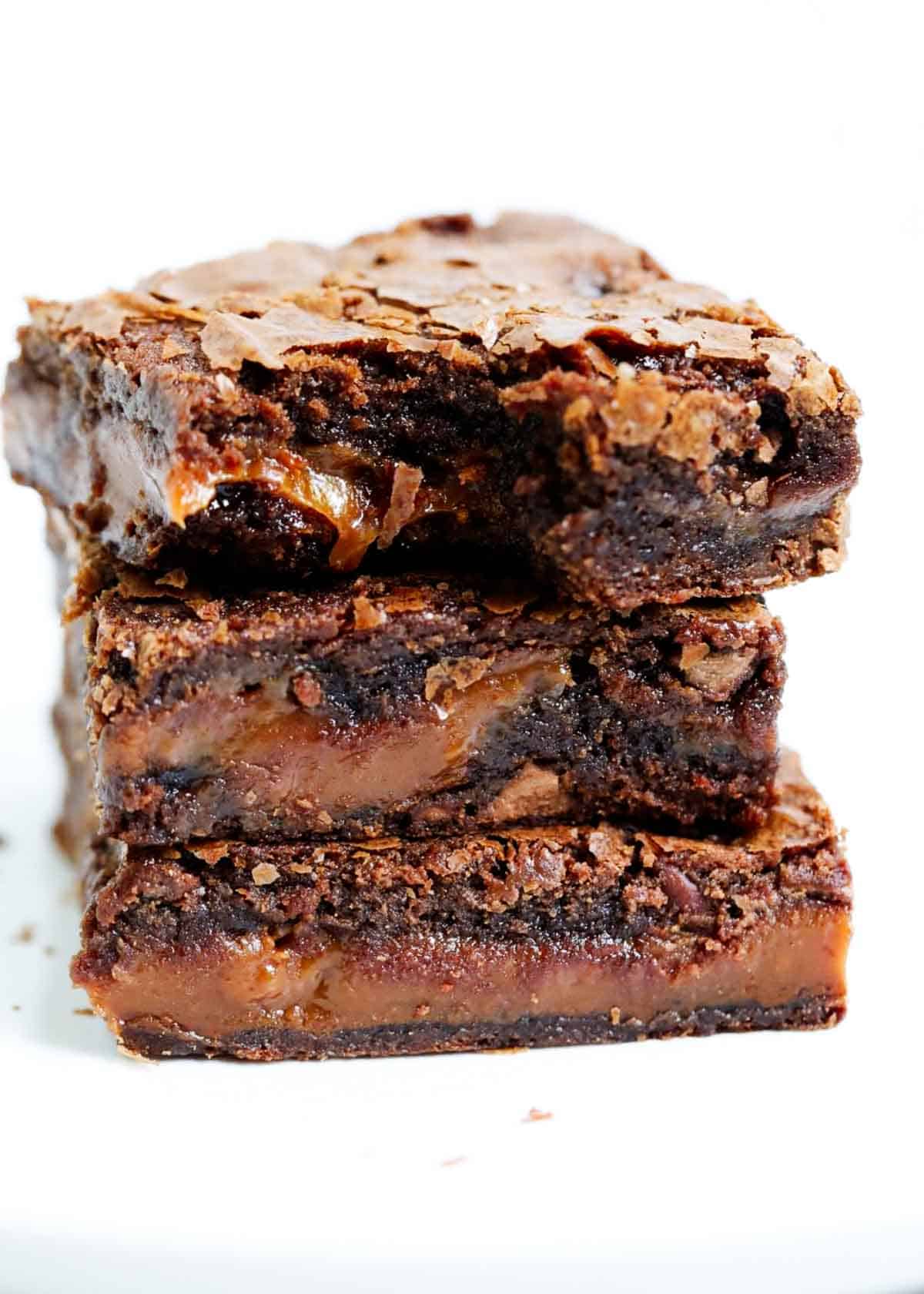 Caramel brownies stacked on top of each other with a bite taken out of the top brownie.