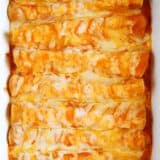 Cheese enchiladas smothered in enchilada sauce and cheese in a white baking dish.