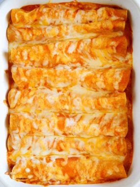 Cheese enchiladas smothered in enchilada sauce and cheese in a white baking dish.